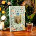 Dilmah-adventskalender med te og et blomstret omslag ved siden af en glaskop med te