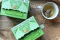 Two green Friday Afternoon boxes on a wooden tray, the front one labeled 2026 Tea Advent Calendar, Decaffeinated, Pyramid Teabag, beside a cup with a pyramid bag.