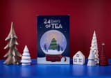 Adagio Teas 24 Days of Tea Kalender neben kleinen Holzbäumen und Häusern