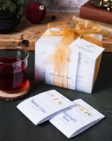 Calendrier ArtfulTea avec un ruban doré près d'enveloppes Masala Chai et d'un verre
