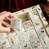 Hand hält einen Würfel aus dem New English Teas Kalender über dem nummerierten Raster