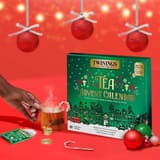 Hand hält eine Tasse Tee neben dem Twinings Brew Joy Together Kalender