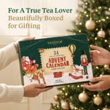 Mains tenant le coffret cadeau calendrier de l'Avent Vahdam 2026 près d'un sapin de Noël
