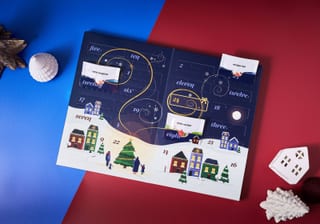 Geöffneter Adagio Teas Schneekugel-Adventskalender 2026 mit illustrierten Dorftürchen