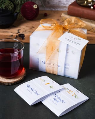 Calendrier ArtfulTea avec un ruban doré près d'enveloppes Masala Chai et d'un verre