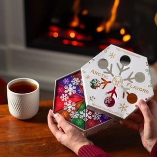Hände heben am Kamin den Deckel einer sechseckigen Nordqvist-Winterteeschachtel, auf dem Tisch steht eine Tasse Tee
