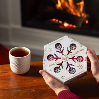 Hände halten die geschlossene Nordqvist Arctic Flavors Box neben einer Tasse