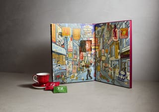 Geöffneter T2 x Kentaro Yoshida Kalender auf grauem Hintergrund mit roter Tasse