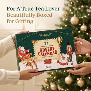 Mains tenant le coffret cadeau calendrier de l'Avent Vahdam 2026 près d'un sapin de Noël