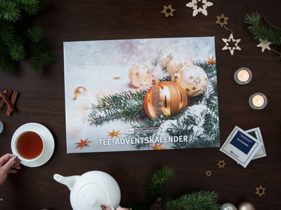 Flat TeeGschwendner advent calendar of numbered doors over gold baubles and fir, with a Salzcaramel sample packet, a teapot and a cup of tea.