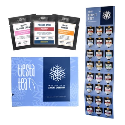 Blue Tiesta Tea box labeled 24 Day Loose Leaf Tea Advent Calendar, with snowflakes and pouches including Nutty Almond Cream, Fireside Spice and Maui Mango, some marked caffeine free, beside a Keep It Cozy board of pouches.