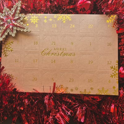 Kraft advent calendar with gold snowflakes, gold door numbers and the words Merry Christmas, lying on red tinsel.
