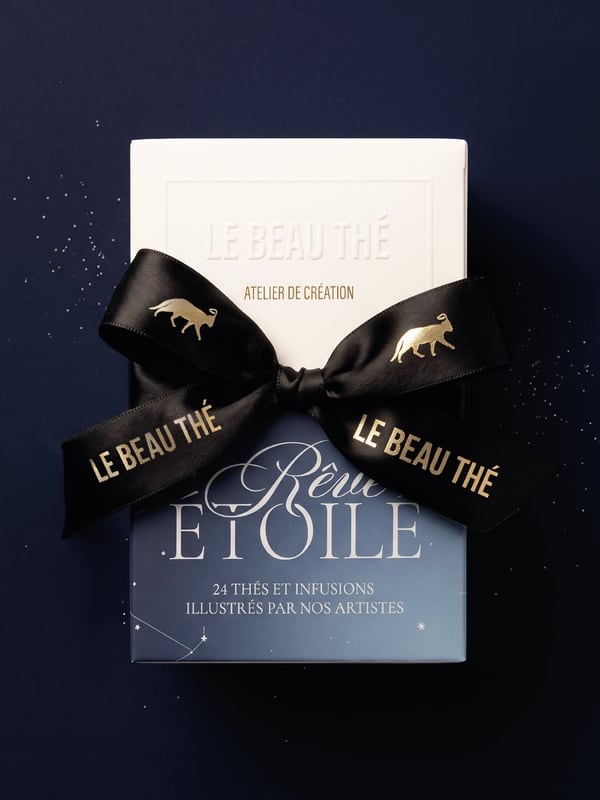 White Le Beau Thé box stacked on a blue Rêve Étoile box labeled 24 thés et infusions, with a black ribbon patterned with gold animals.