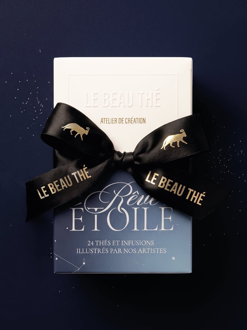 White Le Beau Thé box stacked on a blue Rêve Étoile box labeled 24 thés et infusions, with a black ribbon patterned with gold animals.