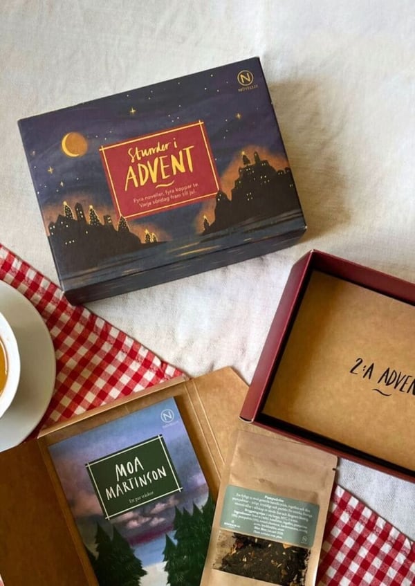 Night-sky box labeled Stunder i advent, Fyra noveller, fyra koppar te, with an open red box marked 2:a adventen, a Moa Martinson booklet, one tea pouch and a cup on gingham.