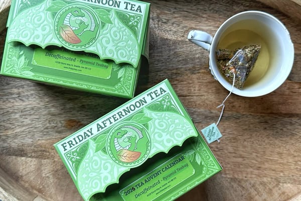 Two green Friday Afternoon boxes on a wooden tray, the front one labeled 2026 Tea Advent Calendar, Decaffeinated, Pyramid Teabag, beside a cup with a pyramid bag.